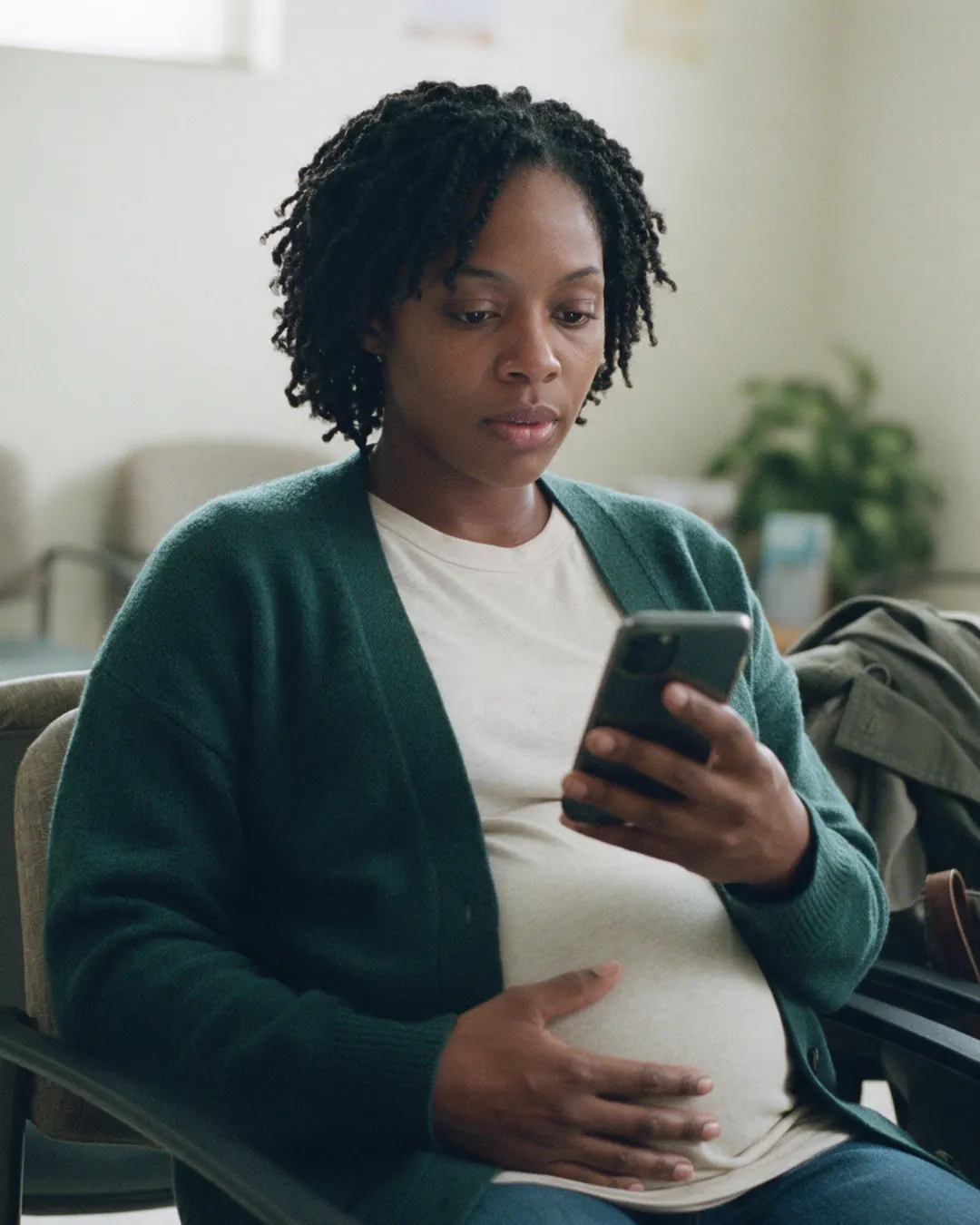 A pregnant woman reviews her phone in a clinic waiting room before her appointment.