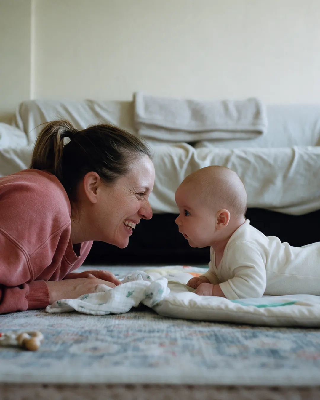 A mother lies on the rug face to face with her baby during tummy time.